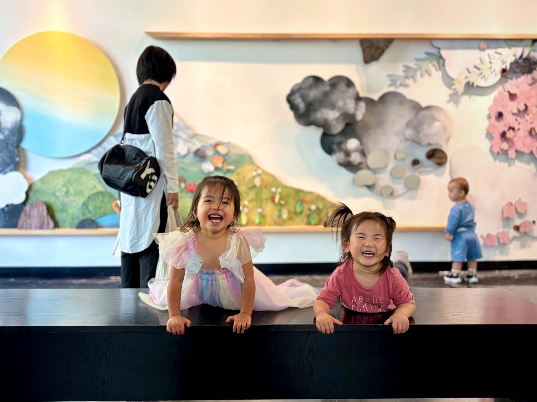 Two young children smile together while families explore the Tend the Garden installation behind them.