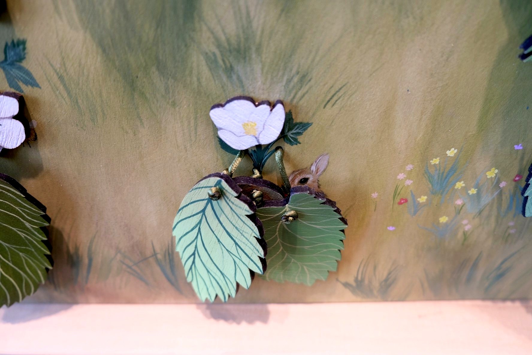 A painted rabbit peeks from behind layered green leaves and a white flower in the sculpture.