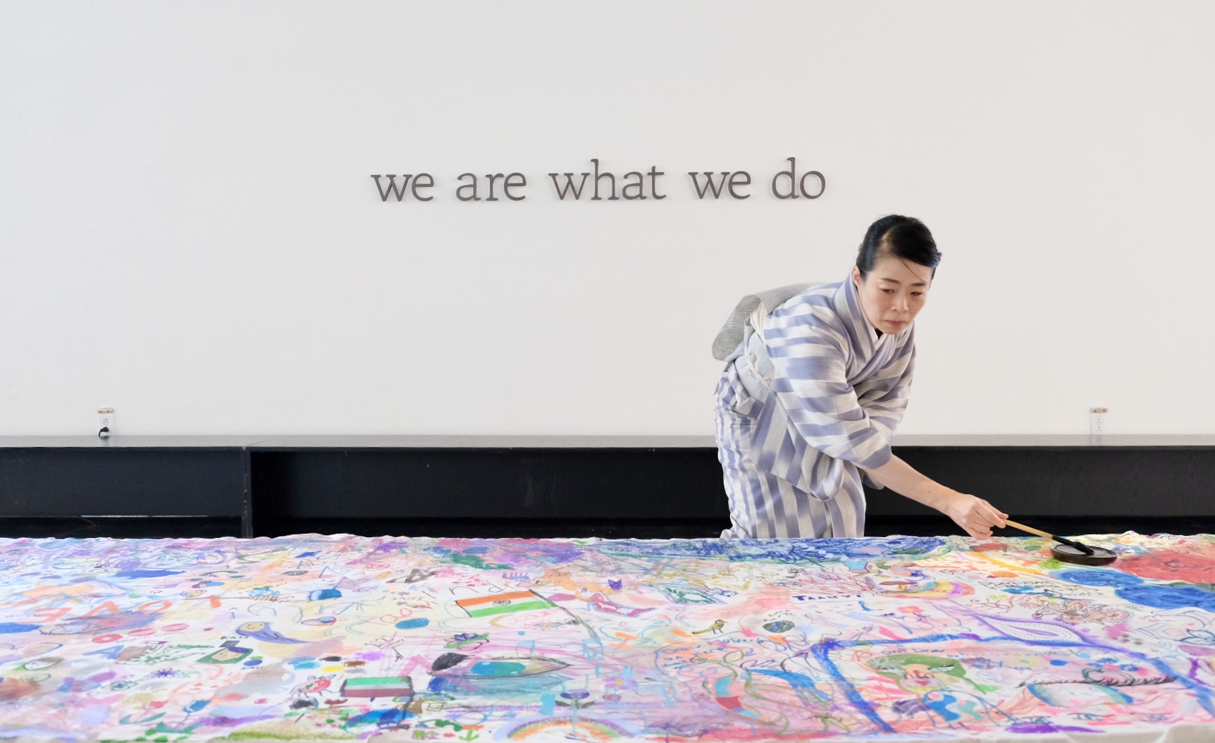 Shizu Usami adds the final mark to the collaborative canvas beneath the words We are what we do.