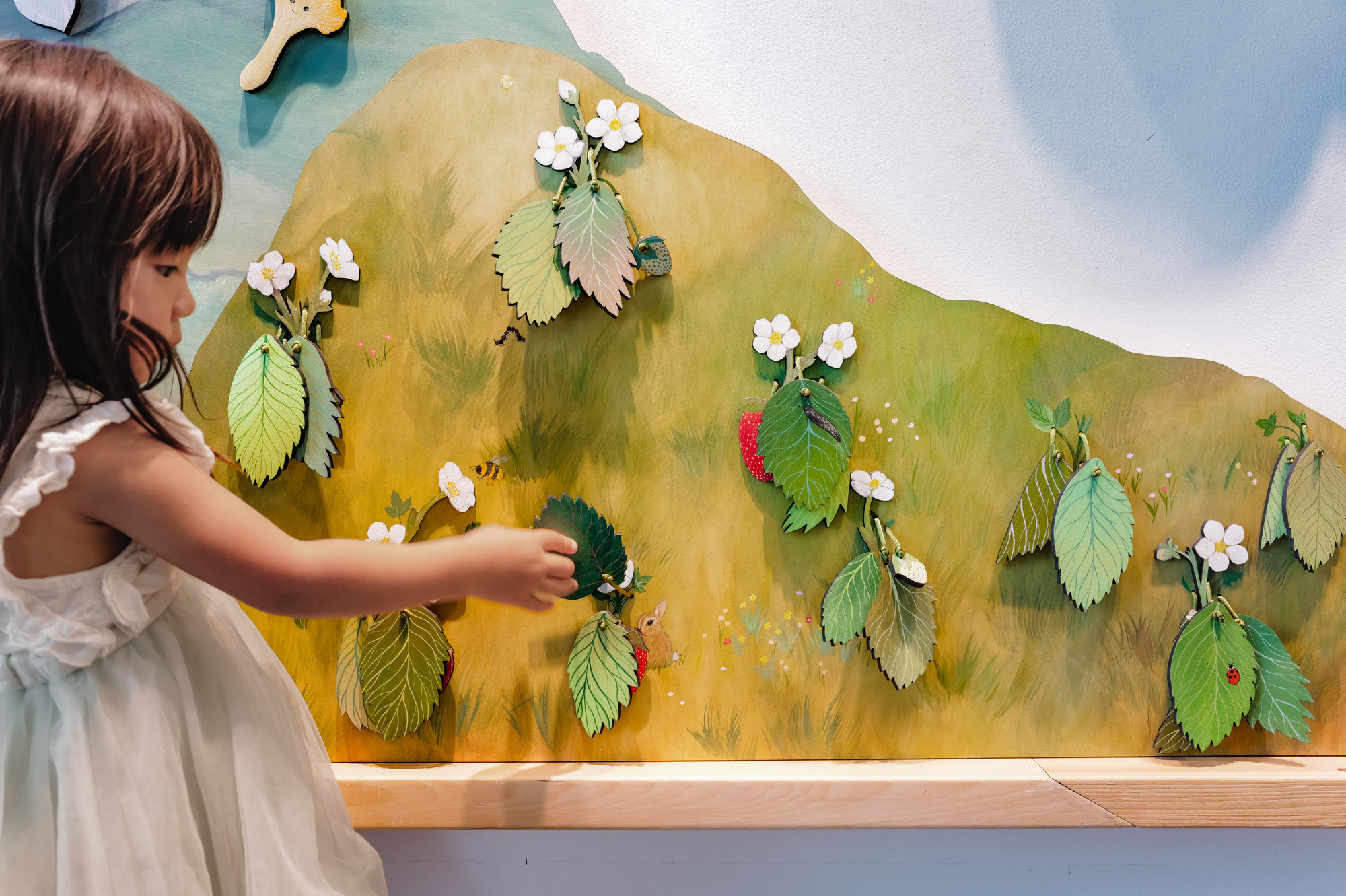 Haru lifts a layered painted leaf in the strawberry patch to unveil a hidden bunny.